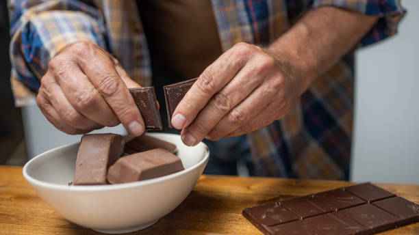 Man hands breaking chocolate Senior man hands breaking chocolate bar and putting pieces in bowl close up man hand holding candy bar stock pictures, royalty-free photos & images