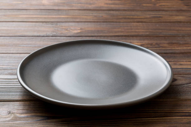 istock Perspective view of empty black plate on wooden background. Empty space for your design 1818064427