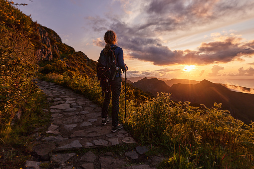 Rear view of a female hiker looking at view while standing on a mountain at sunset. Copy space.