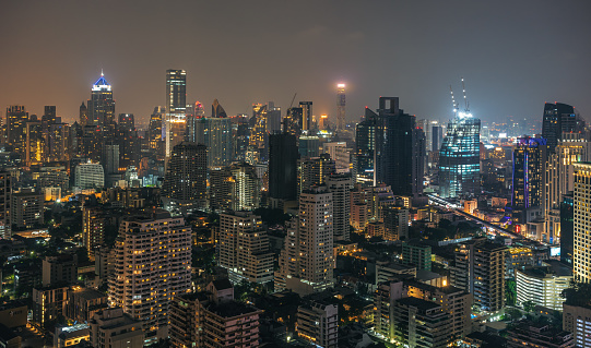 Bangkok, Thailand - March 15, 2023: Night urban cityscape skyline panorama of modern illuminated city with glowing skyscrapers and buildings in dusk. High-angle view on metropolis lights in twilight