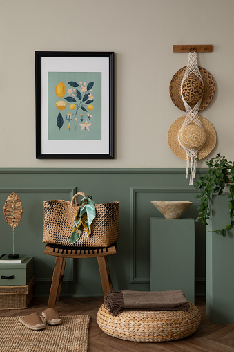 Spring composition of warm living room interior with mock up poster frame, wooden stool, braided bag, hat, stylish macrame, green stands, slippers and personal accessories. Home decor. Template.