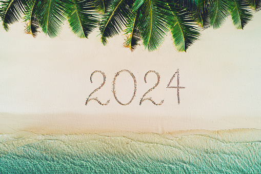 Happy new year beach concept, 2024 written on the sand. Summer holiday on tropical island. Palm trees and sea waves.