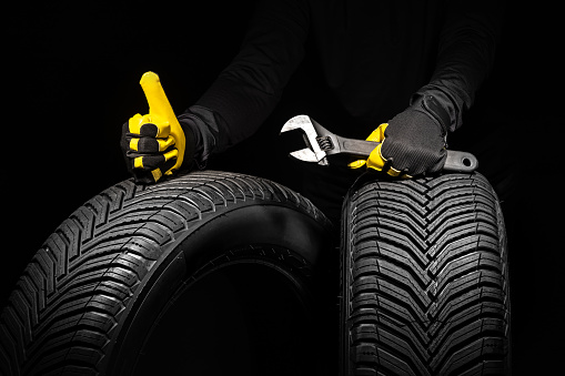 Winter car tires service and thumbs up hands of mechanic with wrench, screwdriver on black background.