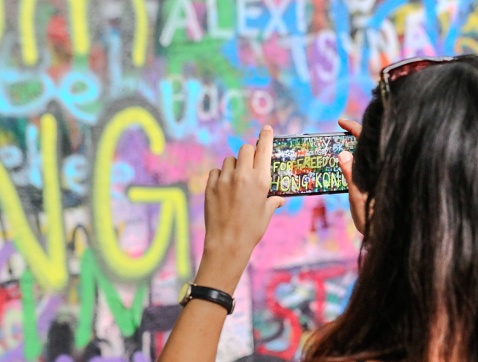 Prague, Czech Republic – August 18, 2019: A young female photographer taking a photograph of a colorful graffiti mural painted on the side of an urban wall