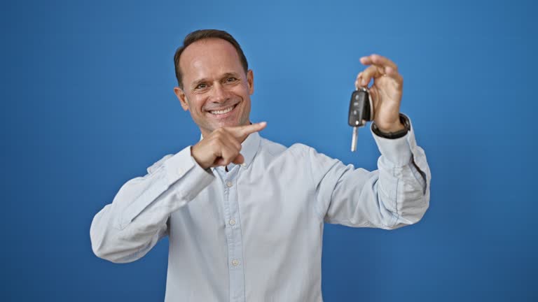 Confident middle age man joyfully celebrating his win, confidently pointing to new car key, radiating positivity and joy, isolated on white background