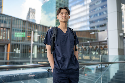 An Asian male wearing medical scrubs in an urban setting