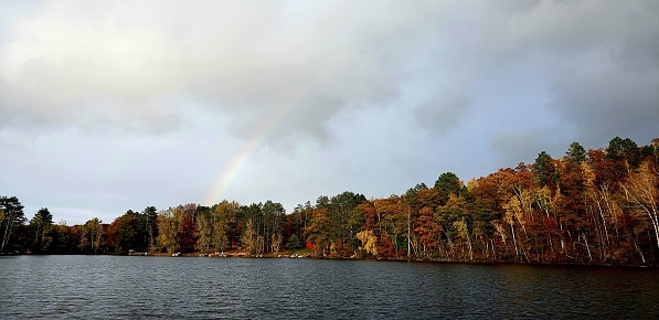 The tranquil lake lined with autumn trees against the backdrop of a sky with a rainbow