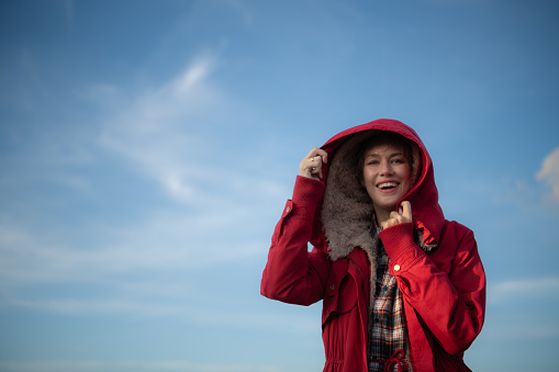 Portrait of a beautiful young woman in red coat on the background of blue sky