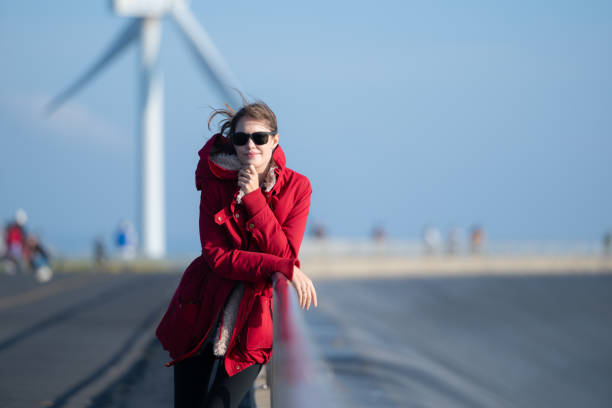 On the background of windmills, A young woman in a red jacket is enjoying her winter vacation.