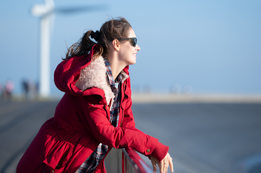 On the background of windmills, A young woman in a red jacket is enjoying her winter vacation.