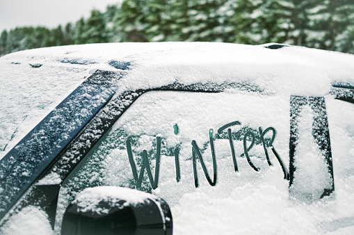 a word Winter written by hand on a car covered with snow, daylight shot