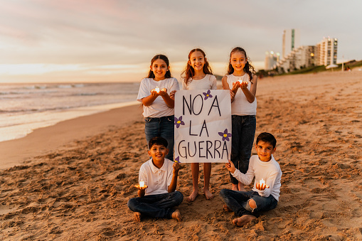Portrait of child friends protesting against the war (with a Spanish message o stop war) on the beach