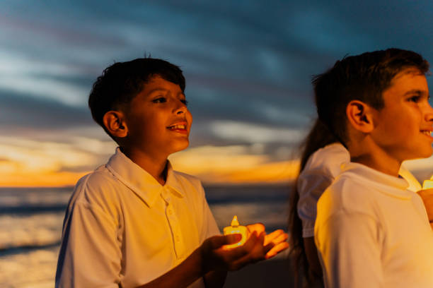 Child boy looking away and holding a candle on the beach