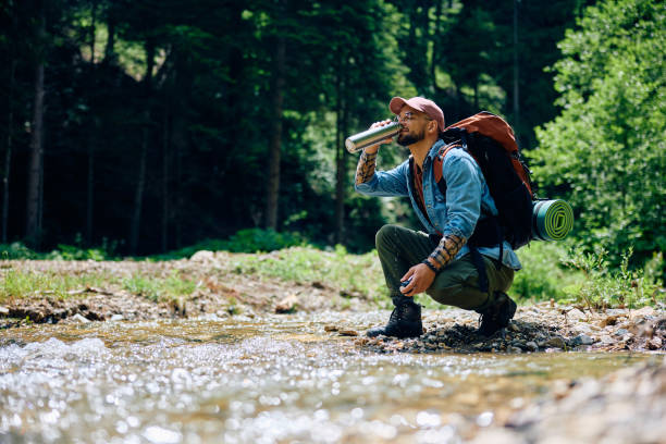 Young hiker drinking water from mountain creek.