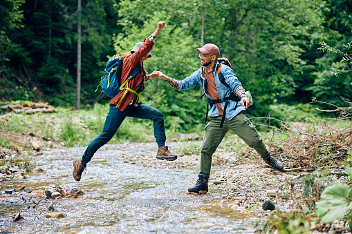 Couple of hiker having fun while jumping over the stream in nature. Copy space.