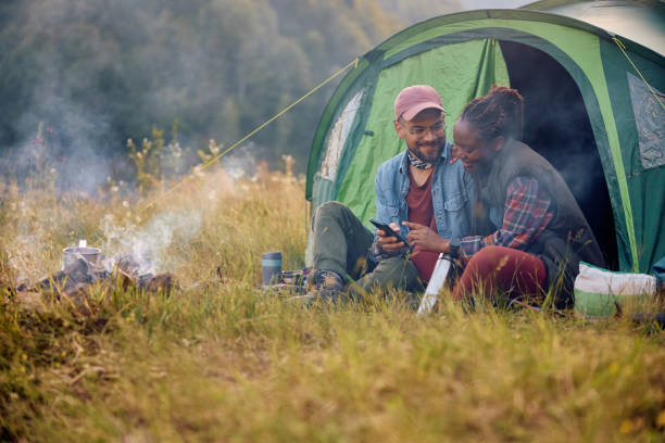 istock Happy multiracial couple using cell phone while camping in nature. 1818221388