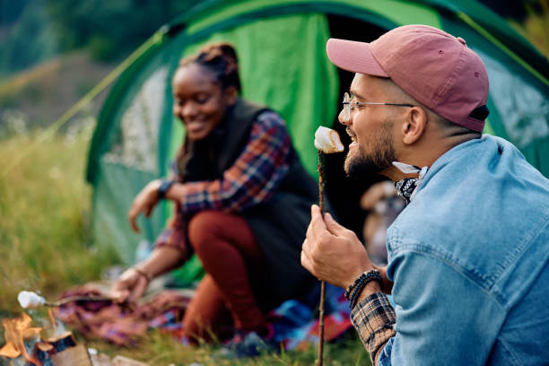 istock Happy man tasting roasted marshmallow while camping with girlfriend in nature. 1818221509