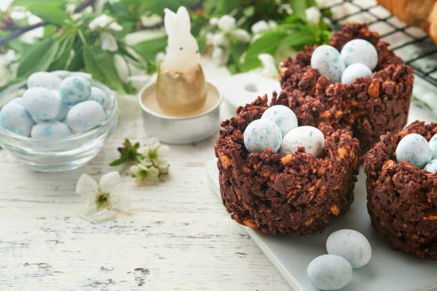 istock Easter brunch or breakfast. Easter chocolate nest cake with chocolate candy eggs, traditional hot cross buns and deviled eggs with bouquets of blooming apple trees. Spring Easter holiday food concept. 1818222061