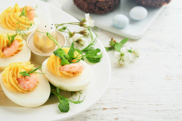 istock Stuffed or deviled eggs yolk, shrimp, pea microgreens with paprika for easter table decorate fresh cherry or apple blossoms on white light background. Happy Easter traditional dish concept. Mock up. 1818222085