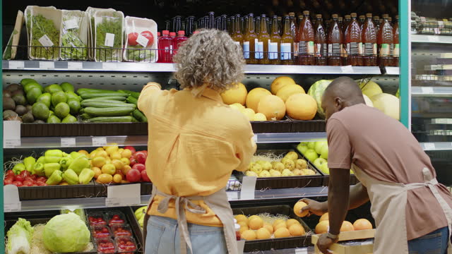 Diverse Shelf Fillers Laying Out Fruit and Vegetables in Grocery Store