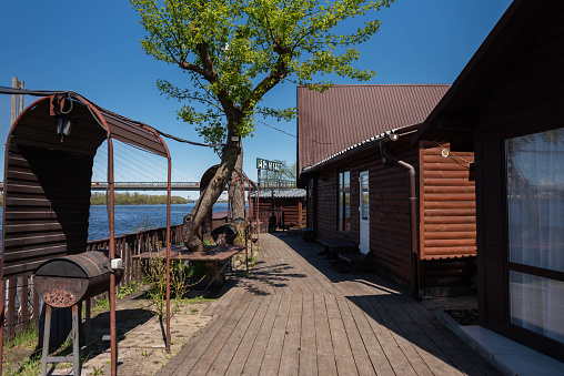 Cafe by the river - wooden terrace, barbecue grill, wooden houses for rest, nature. Country holiday.