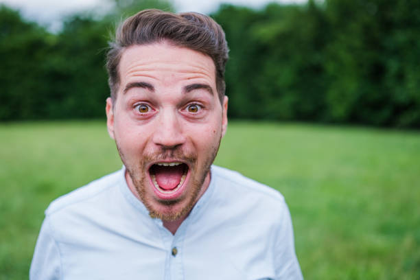 Young man in the park expressing a shocked face and shouting