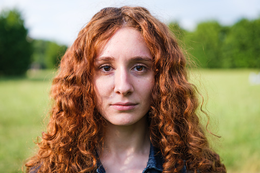 Portrait of young redhead woman with serious face outdoors in the park on a sunset