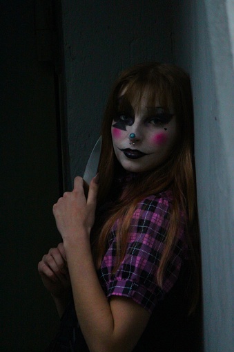 A portrait of a young female with a vibrant and fun clown-painted face holding a knife.