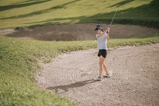 asian chinese female Golfer hitting out of bunker or sand trap