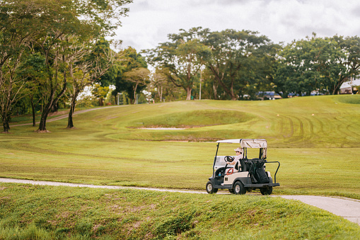 Asian Chinese female golfer driving golf cart in golf course during weekend morning