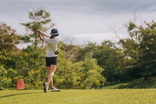 Rear view of asian chinese young female golfer teeing off and swing her driver club on the golf course