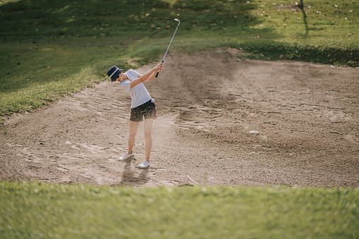 asian chinese female Golfer hitting out of bunker or sand trap