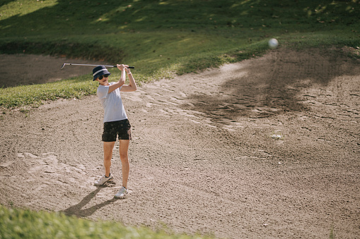 asian chinese female Golfer hitting out of bunker or sand trap