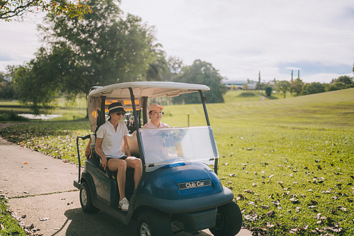 2 Asian Chinese female golfer driving golf cart in golf course weekend morning