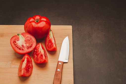 Fresh tomatoes on a wooden cutting board with a knife on a vintage background. Harvesting tomatoes. Top view. Close-up photo. Space for text. Health foods concept