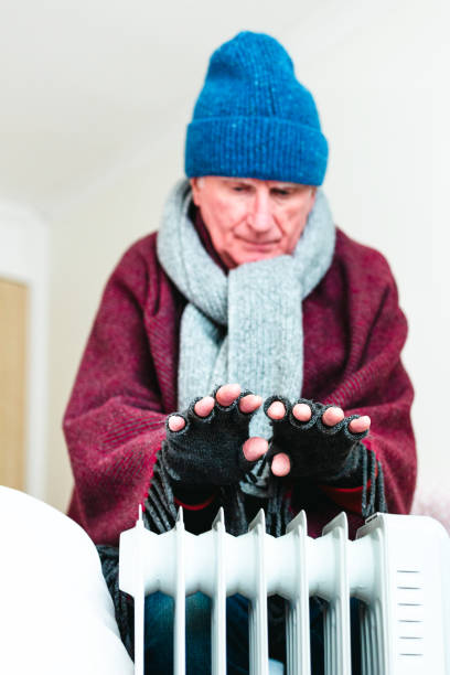 istock Cold senior man warming his hands over electric heater at home 1818277442
