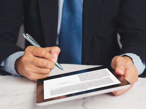 Signature electronic. A Businessman in a suit signing a digital contract or agreement on a tablet while sitting in the office. Business and technology concept