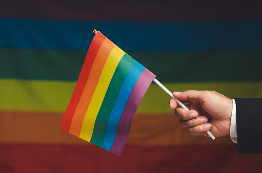 Rainbow flag in hand against a rainbow flag background. Calling on all people to support and respect diversity, gender, and human rights and celebrate LGBTQ Pride month
