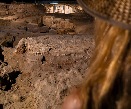 Blond woman with straw hat looking at the ruins and religious wall paintings and frescoes of the saints and the passion of Christ in the crypt of the basements of the church of martyr Saint Eulalia.
