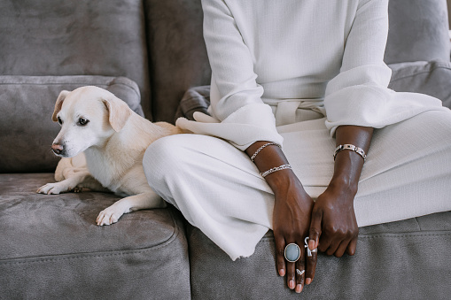 Cropped image of african woman in white traditional clothes sitting on couch with dog, sad mood, companion supports owner. Sad dog with woman at home
