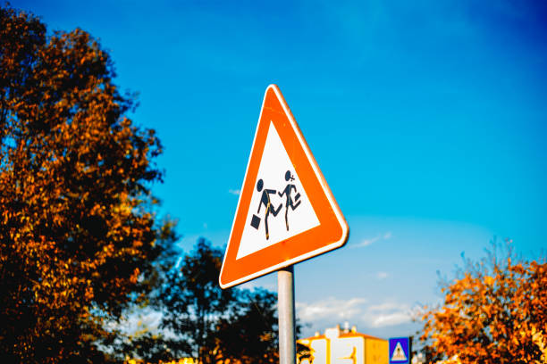 istock Road sign caution children over blue sky background and tree 1818325216