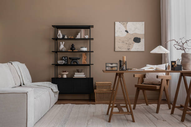 istock Creative composition of warm and cozy workspace interior with mock up poster frame, wooden desk, modular sofa, black rack, rattan chair, stylish lamp and personal accessories. Home decor. Template. 1818326576