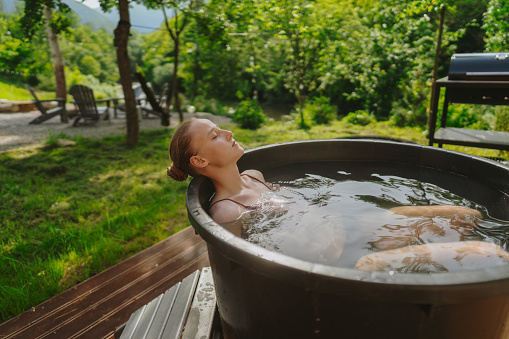 Photo of a young woman having a spa day in the cabin in the woods; she is taking an ice bath after using the sauna