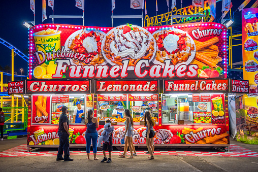 A hungry family attending the Arizona State Fair lines up at a concession stand selling funnel cakes, churros, and lemonade.