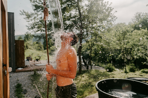 Photo of a young man pouring a bucket of ice cold water over himself, after being in a hot steamy sauna