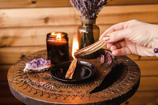 Woman hand holding and using Palo Santo wood sticks smoke for home cleansing session from old negative energy. Oily aromatic holy sacred wood sticks burning in hand.