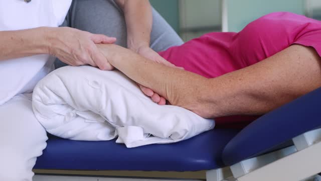 Handheld clip focused on the physiotherapist hands doing a massage to her patient who is recovering from a injury on her arms