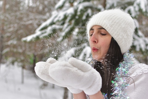 A woman blows on the snow in her hands. Snow in motion. Side view. Space for text.