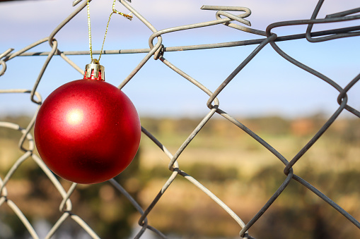 red christmas ball decoration hanging off mesh wire fence in australian summer