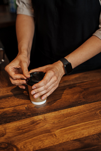 Close-Up of Barista's Hands Sealing Coffee Cup with Lid in Coffee Shop